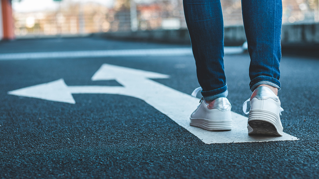 Person walking on lane markings/arrows painted on asphalt.