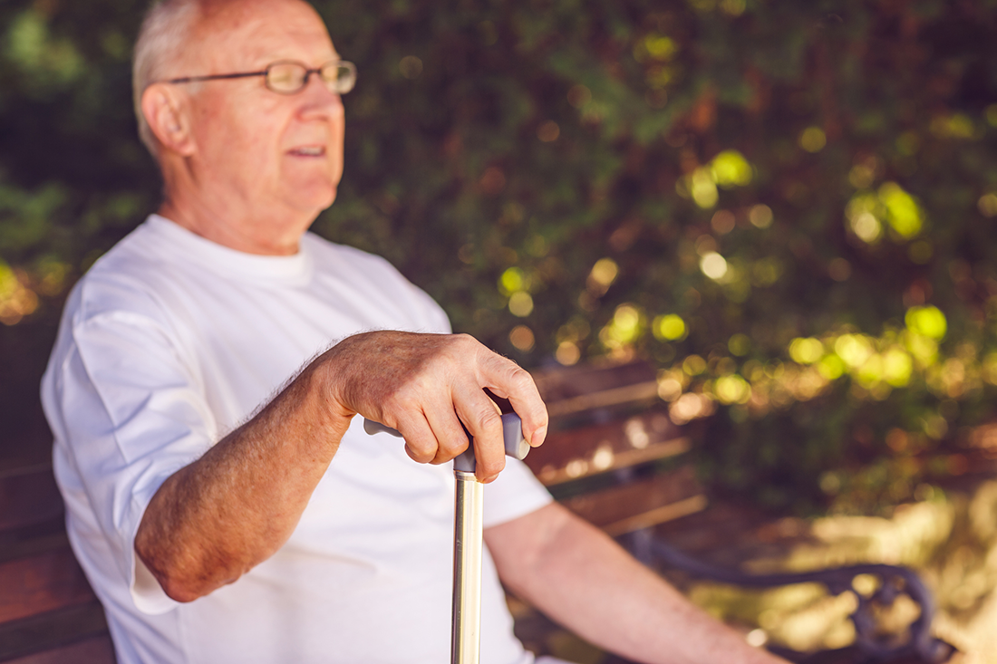 Iäkäs mies puistonpenkillä kävelykeppi kädessään.